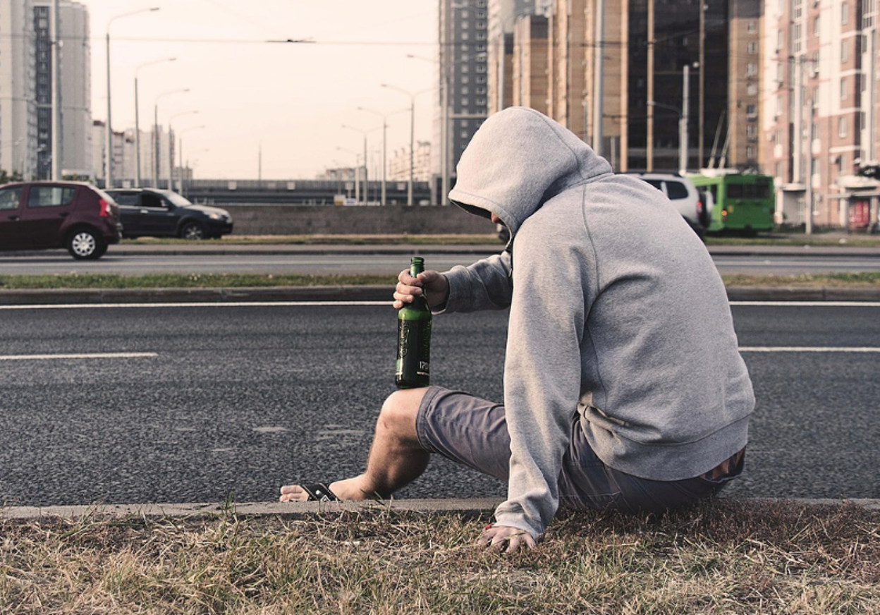 A teen sitting alone holding a drink, looking distressed