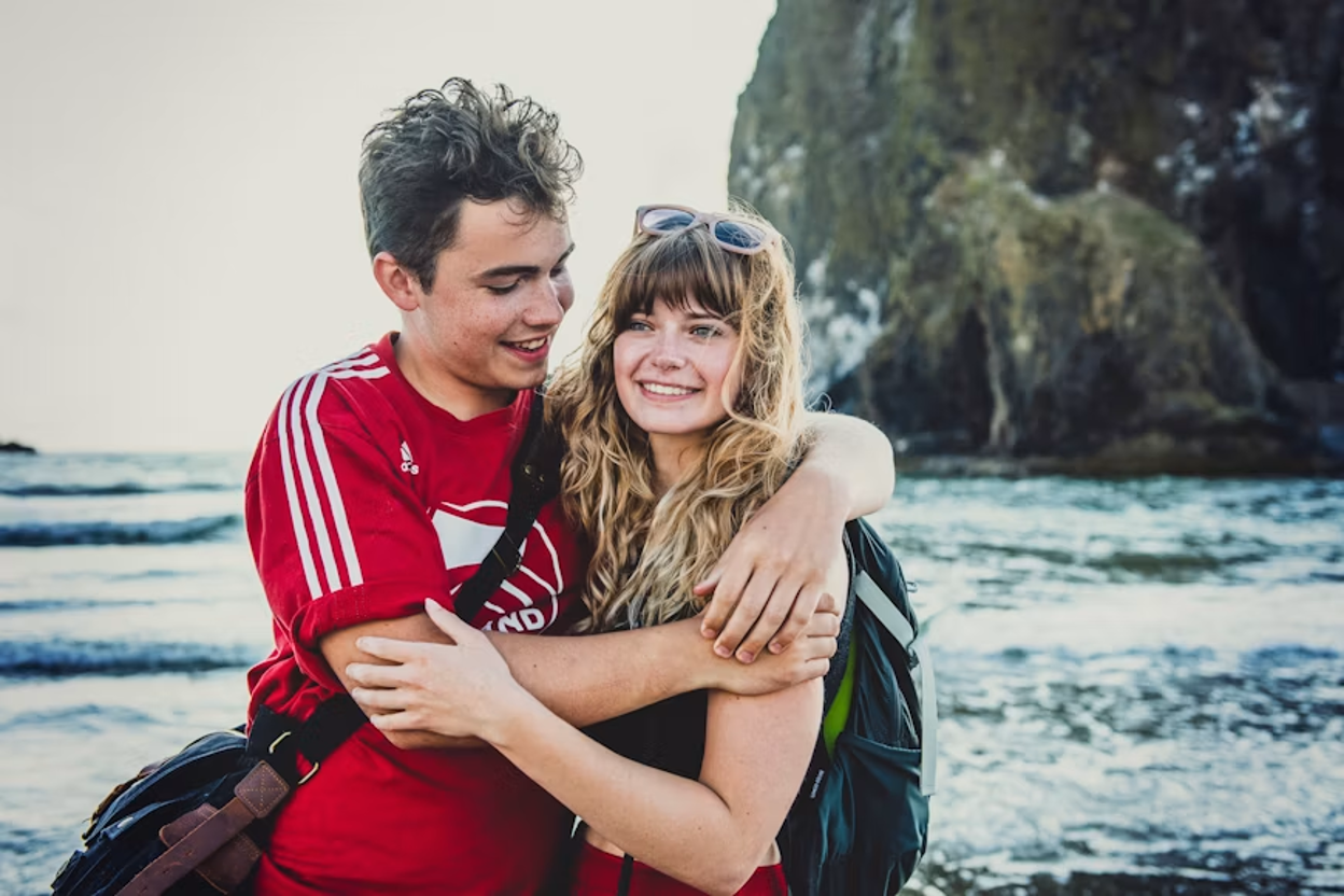 Young teen in a red t-shirt hugging his girlfriend with a beautiful ocean view just behind them
