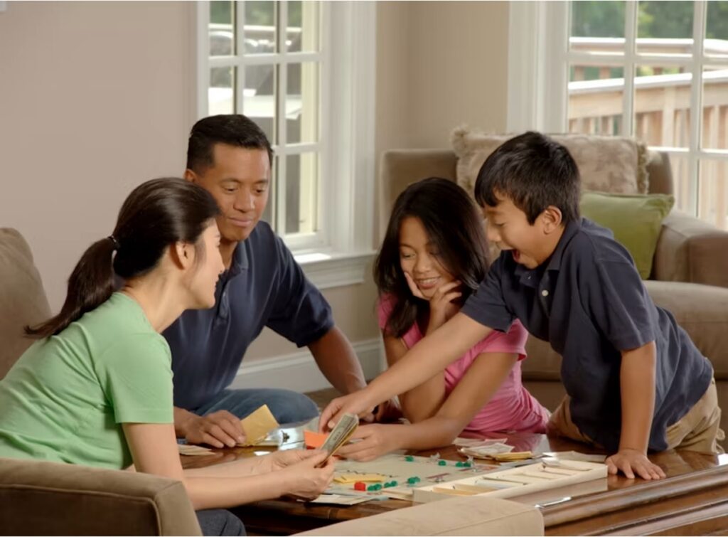 A mother and father sit with their young teen children on a couch, enjoying a game together during a therapy session