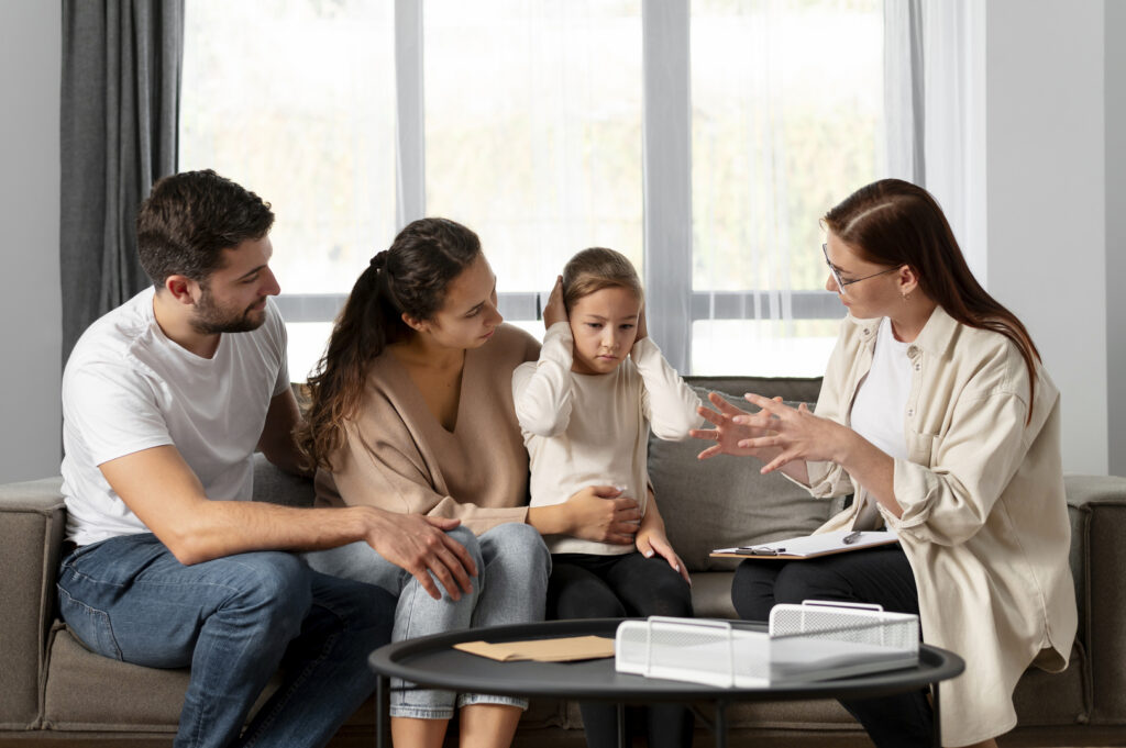A young girl covering her ears while her parents comfort her, and a therapist speaks with the family