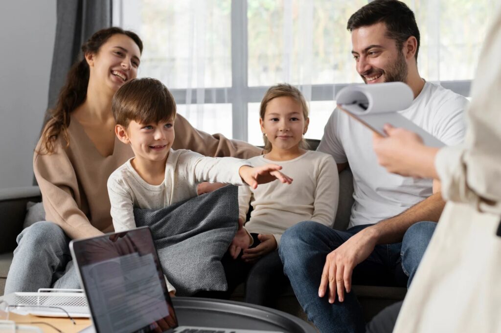 Family of four smiling on a couch during a counseling session while a therapist takes notes