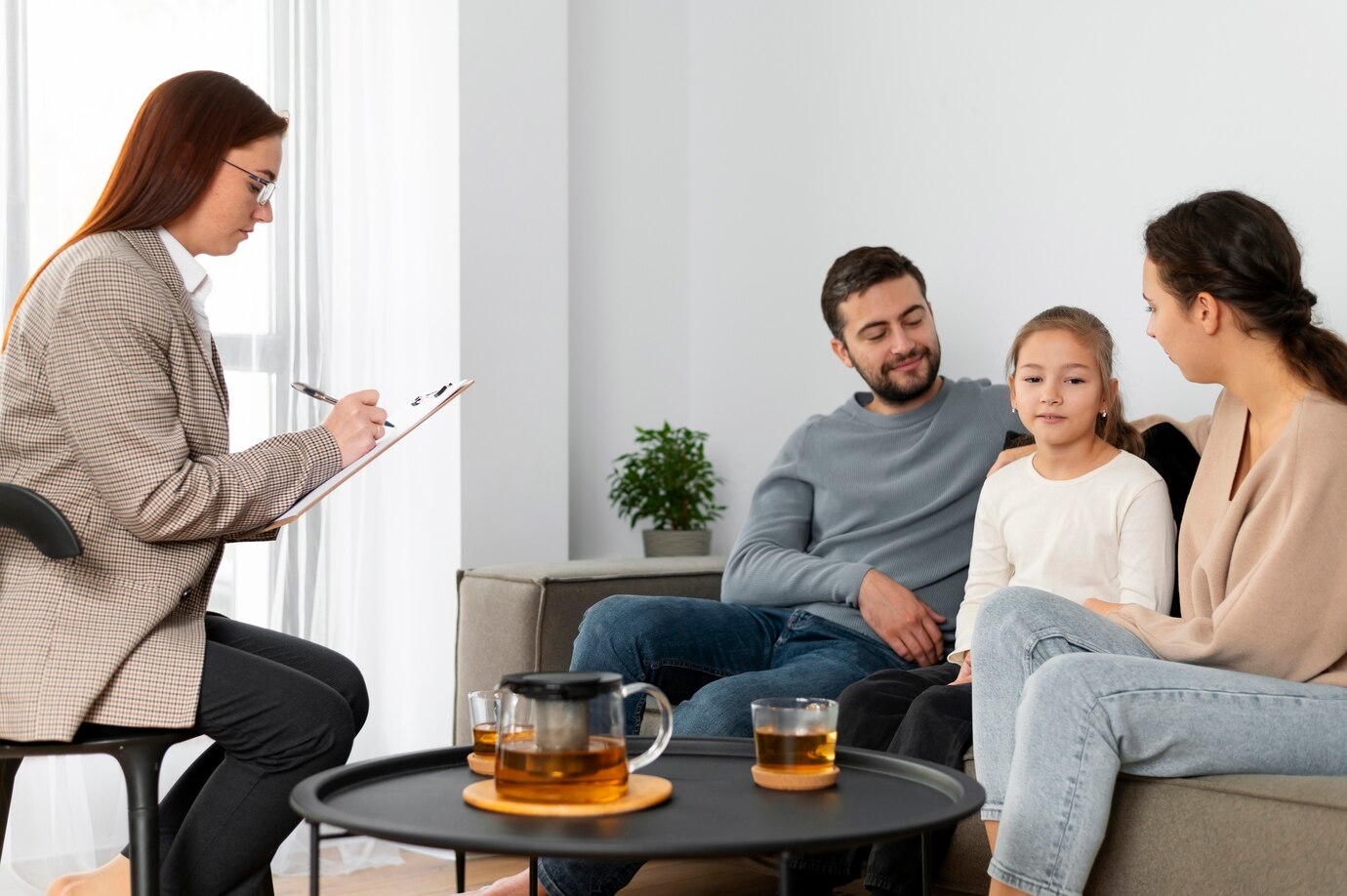 Family therapist taking notes on a clipboard while a couple and their daughter sit together on a couch