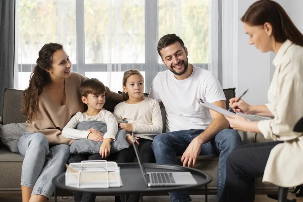 Parents and two children sitting together on a sofa as a female therapist writes on a clipboard