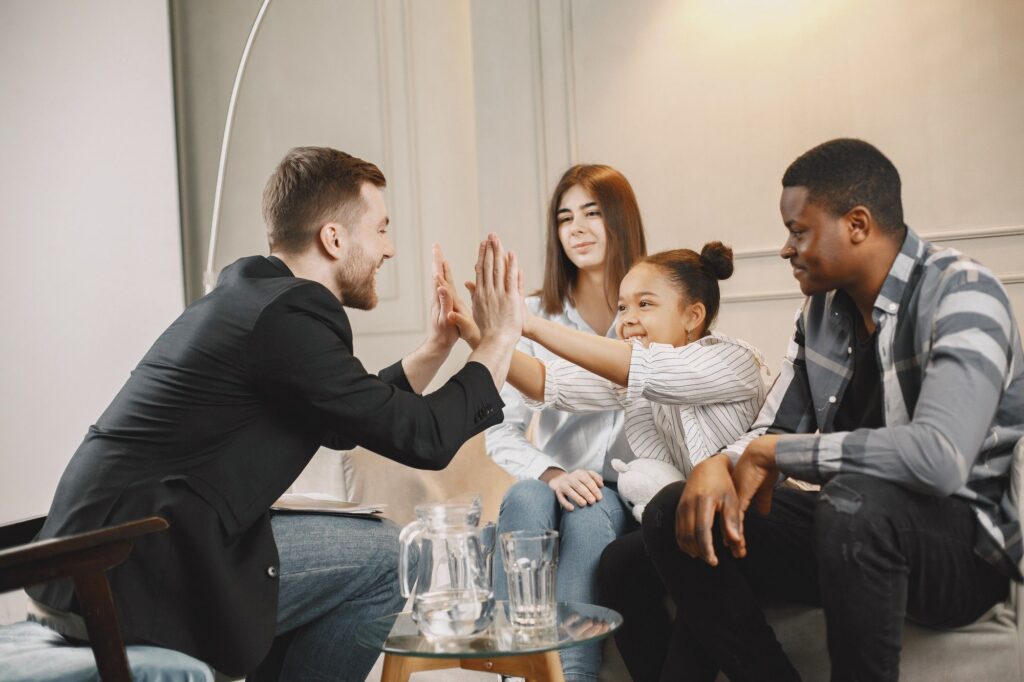 Therapist high-fiving a young girl during a family counseling session as her parents look on