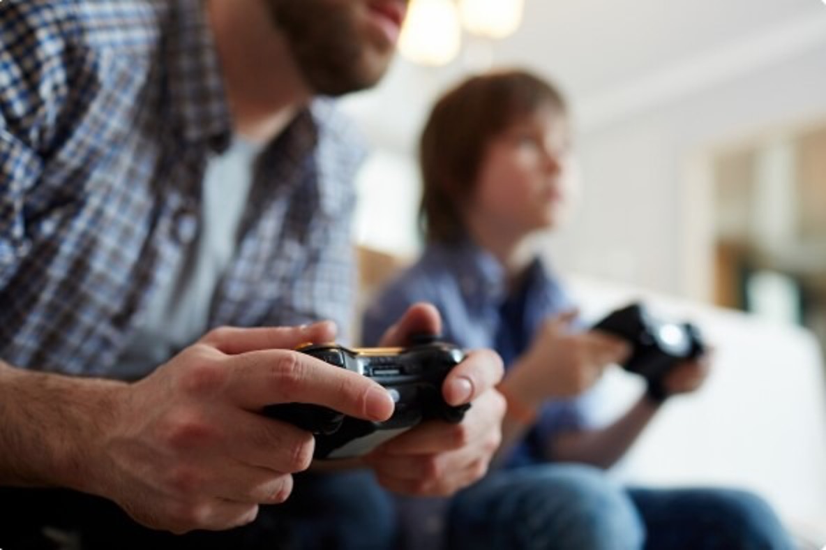 Close-up of a father and son holding game controllers while playing together