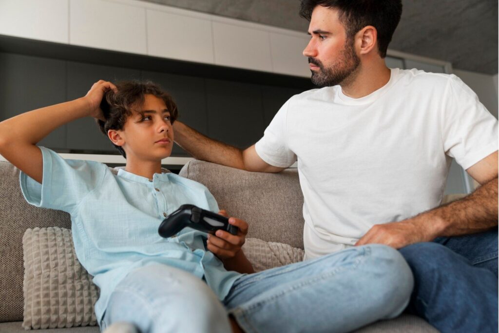 Father placing a reassuring hand on his teenage son's shoulder while the son holds a game controller