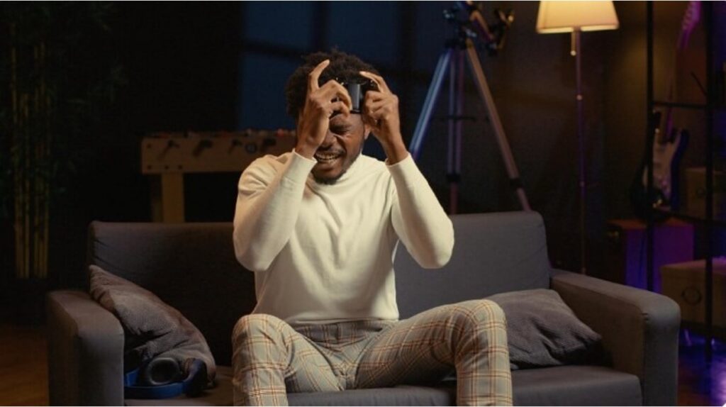 Young man sitting on a couch holding a game controller up to his eyes