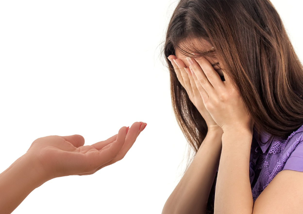 A troubled teen covering their face while having a conversation with their parent