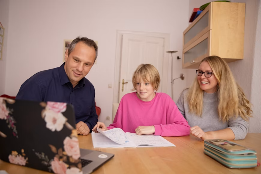 A teen in a pink sweater is being supported by his parents during a homework session