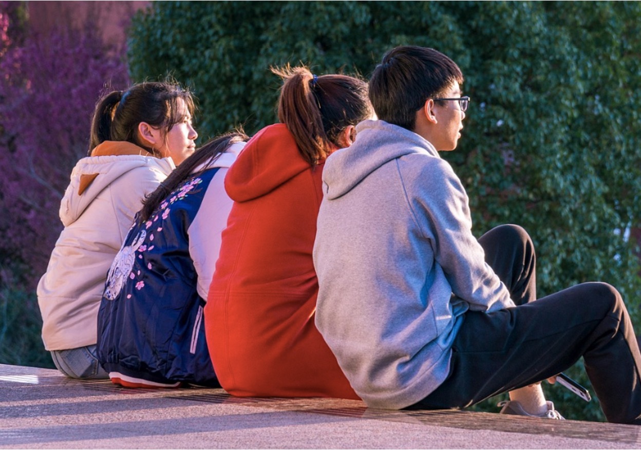 A group of teenagers sitting down on a sidewalk, discussing their problems