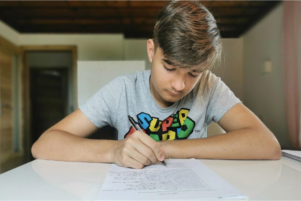 A teenager looking sad while writing, showing stress from academic pressure