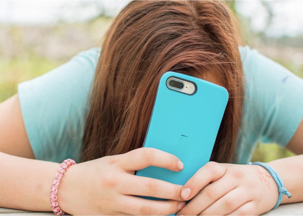 A teenager placing her face in her phone, showing how addictive social media is