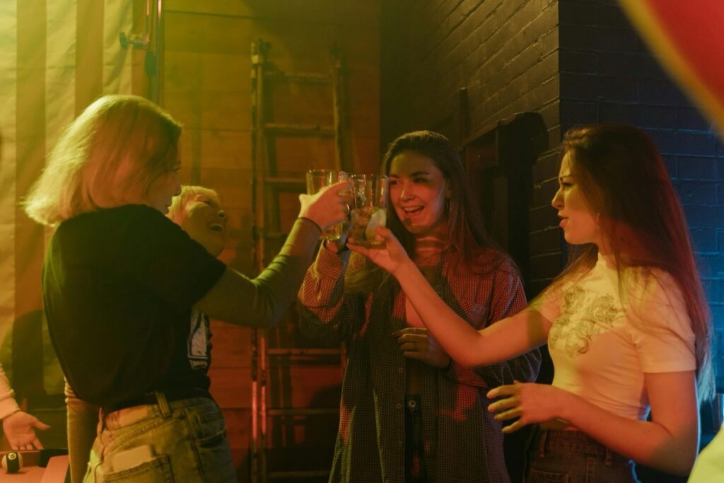 A group of young women raise shot glasses in a toast under colorful party lights