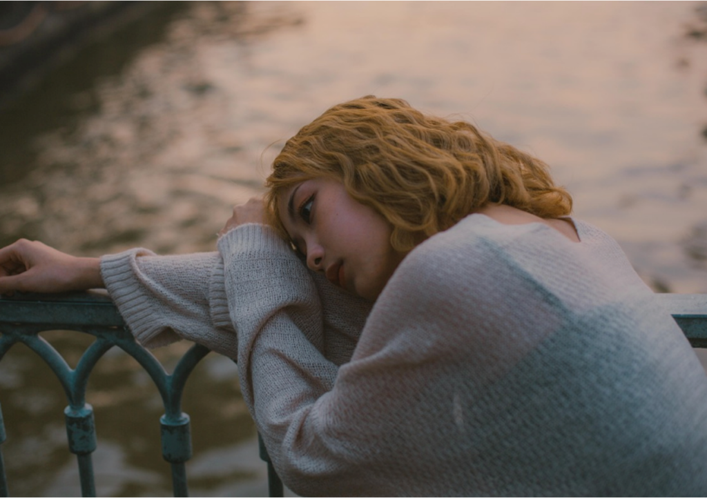 A teenager sitting alone with her head resting on her arm, appearing withdrawn and isolated. 