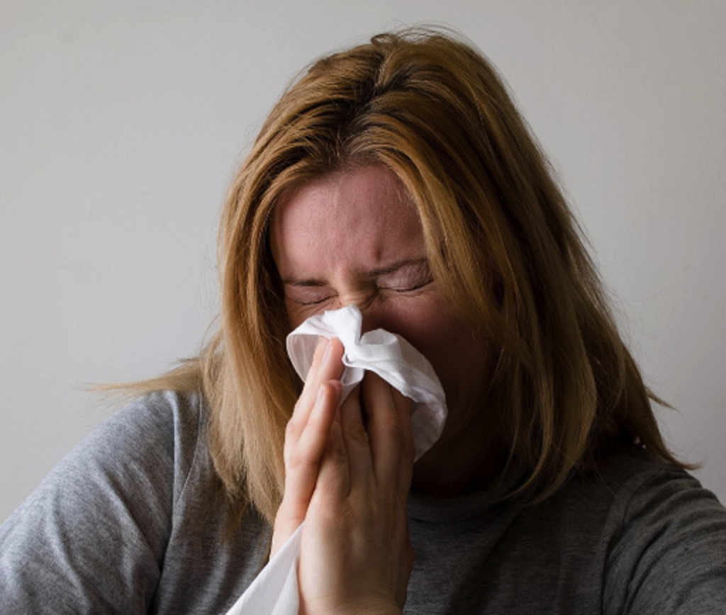 Person blowing nose with a tissue, illustrating flu-like symptoms that can signal opioid withdrawal.