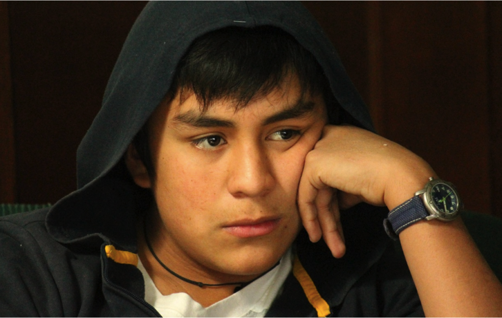 Teenager sitting alone at a table, staring away from friends in the background