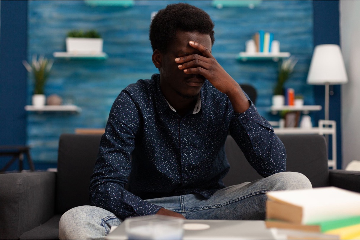 A teenage boy sitting on a couch with his hand covering his face, appearing overwhelmed and emotionally withdrawn