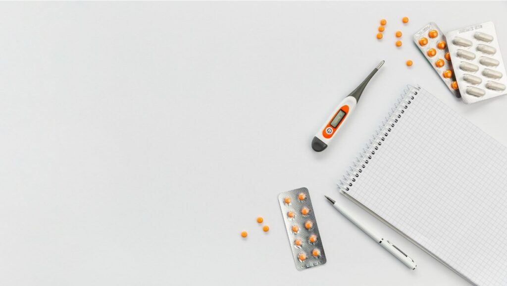 Scattered prescription pills next to an open notebook on a desk.