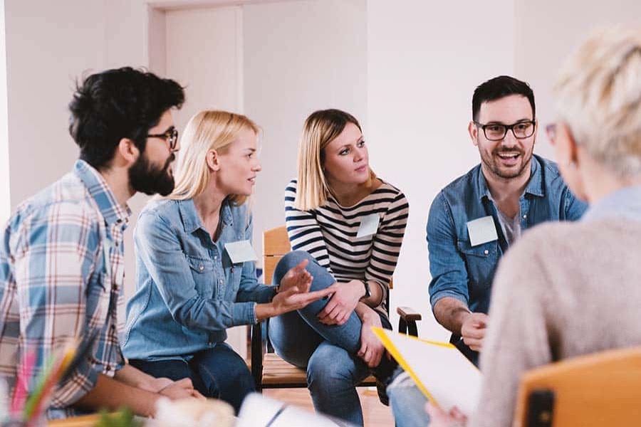 Small group of young adults with name tags leaning in and speaking openly during a peer support group session