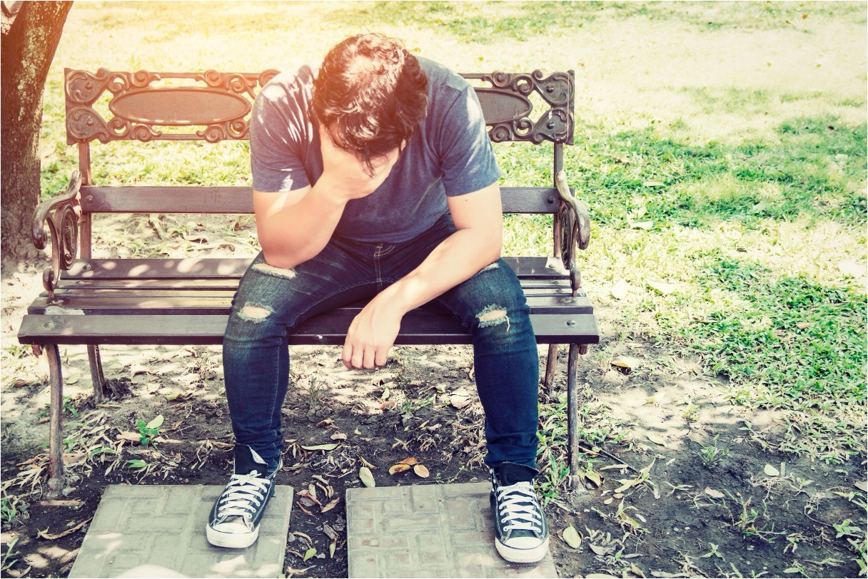 Teenager sitting alone outdoors with head down, representing the emotional toll of mental health struggles and substance use