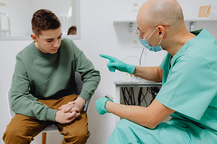A teen sitting with a healthcare professional in scrubs and gloves during a medical consultation