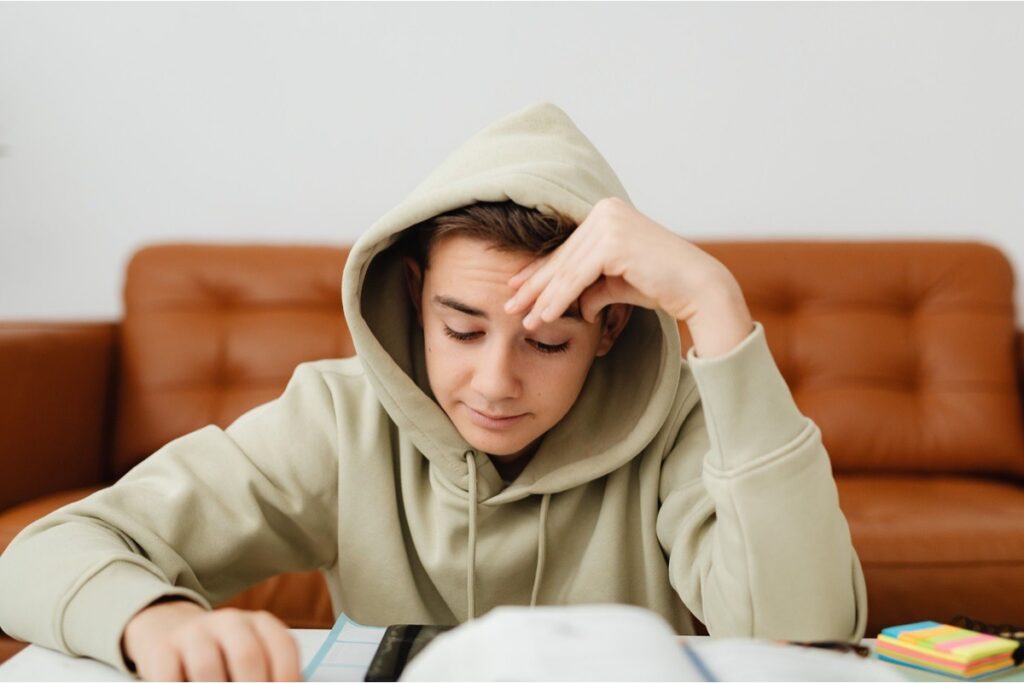 A teen with his head in his hands over homework, showing the daily impact of depression's root causes
