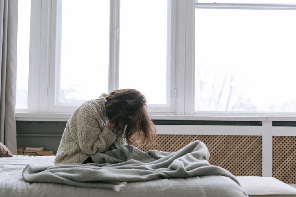 A teenage girl hunched over on her bed in distress, unable to start her day.