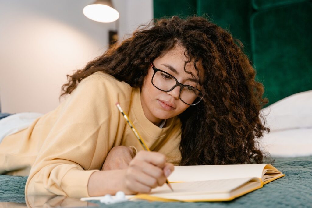 A teenage girl writing in a journal on her bed, tracking patterns related to her panic attacks.
