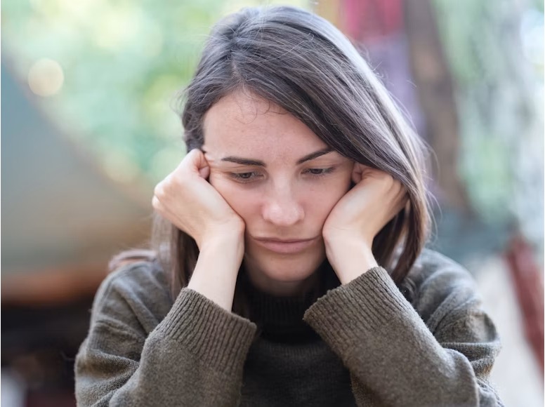 A teenager resting her chin on her fists, looking downward with a sad, contemplative expression