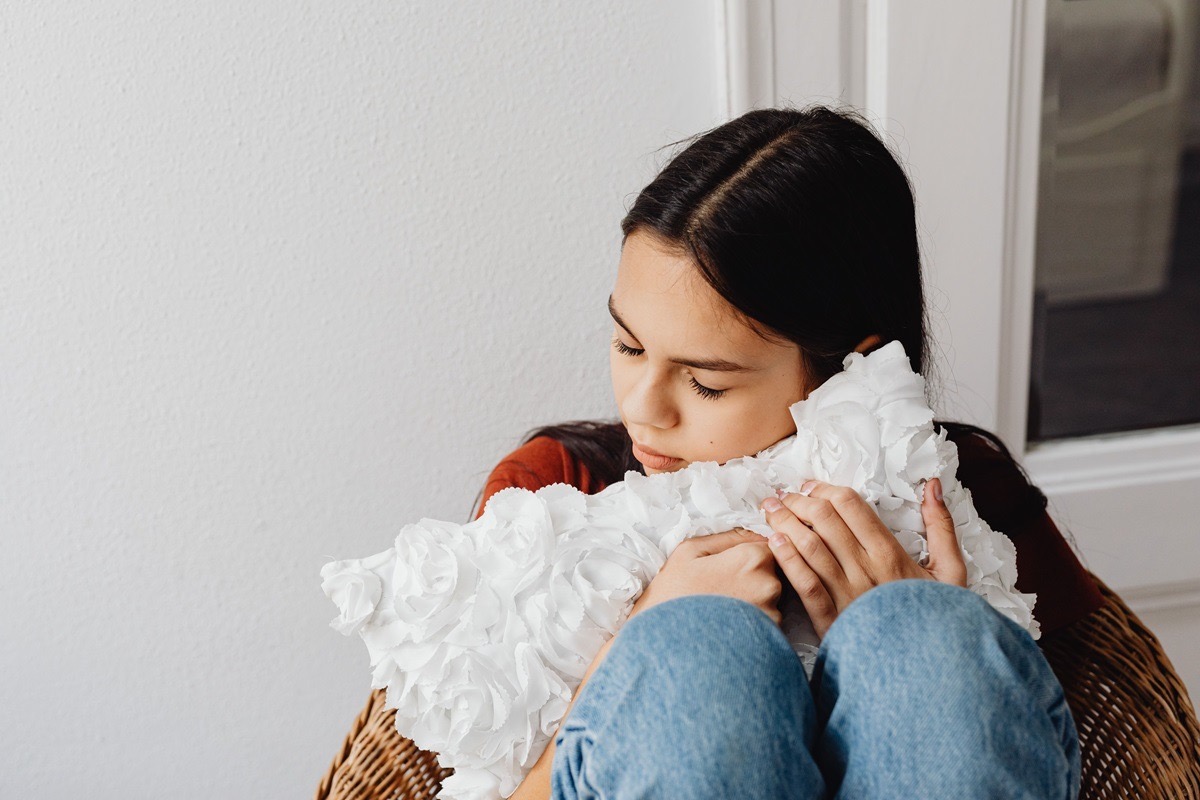 A young teenage girl curled up in a chair holding a pillow, showing the quiet distress of adolescent anxiety