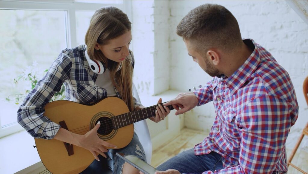 Man teaching a teenage girl how to play acoustic guitar