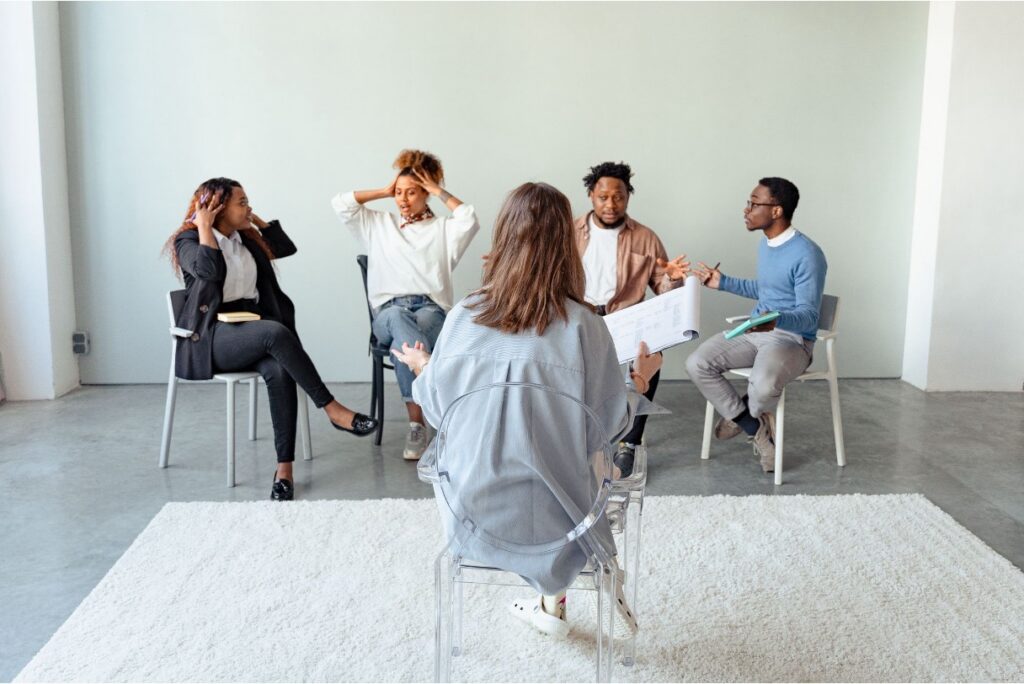 Matured teens in a calming room sitting in a semi circle engaged in a group therapy session with a licensed therapist facilitating the process