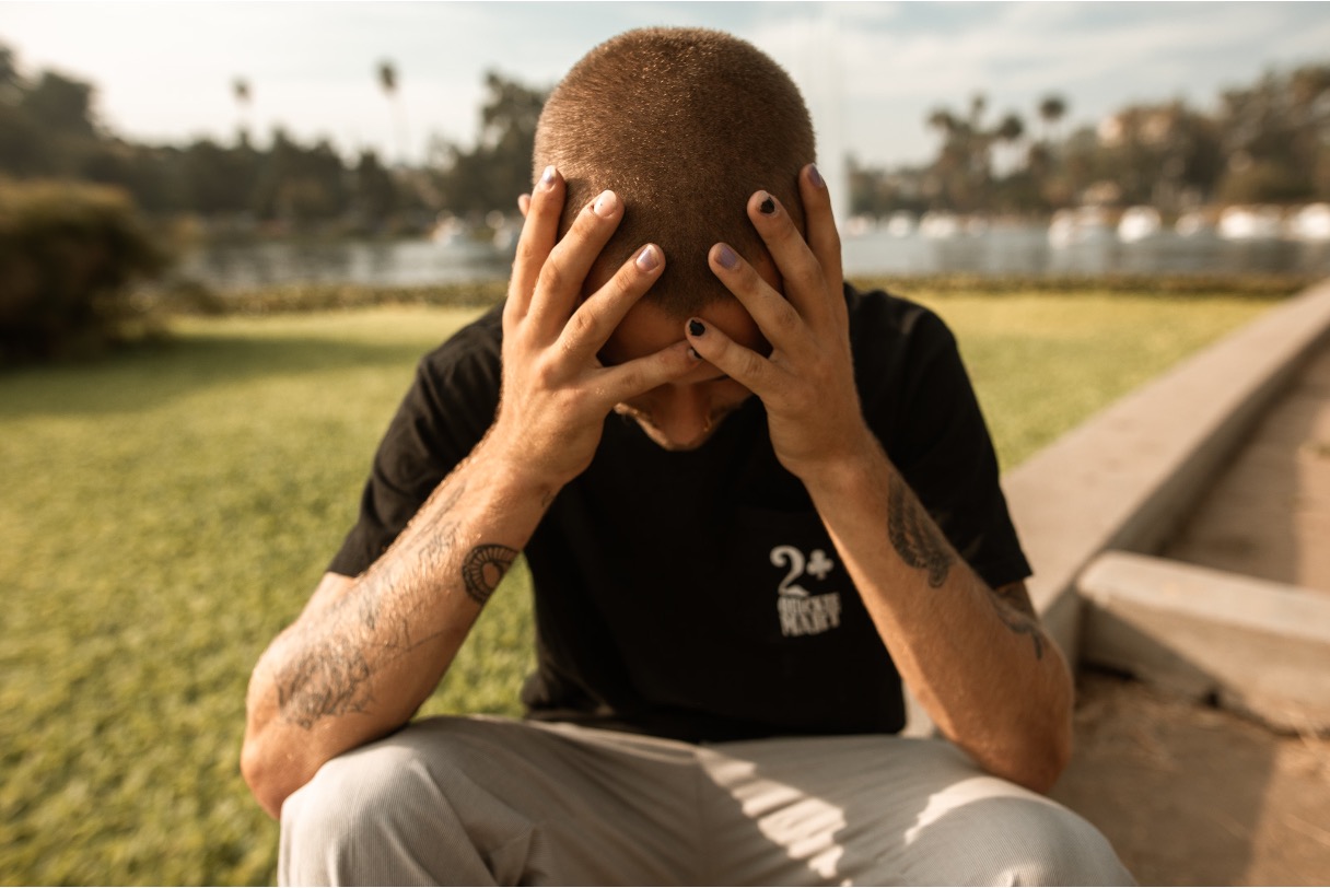 Tattooed teen sitting outdoors, head in hands, conveying emotional distress or overwhelm