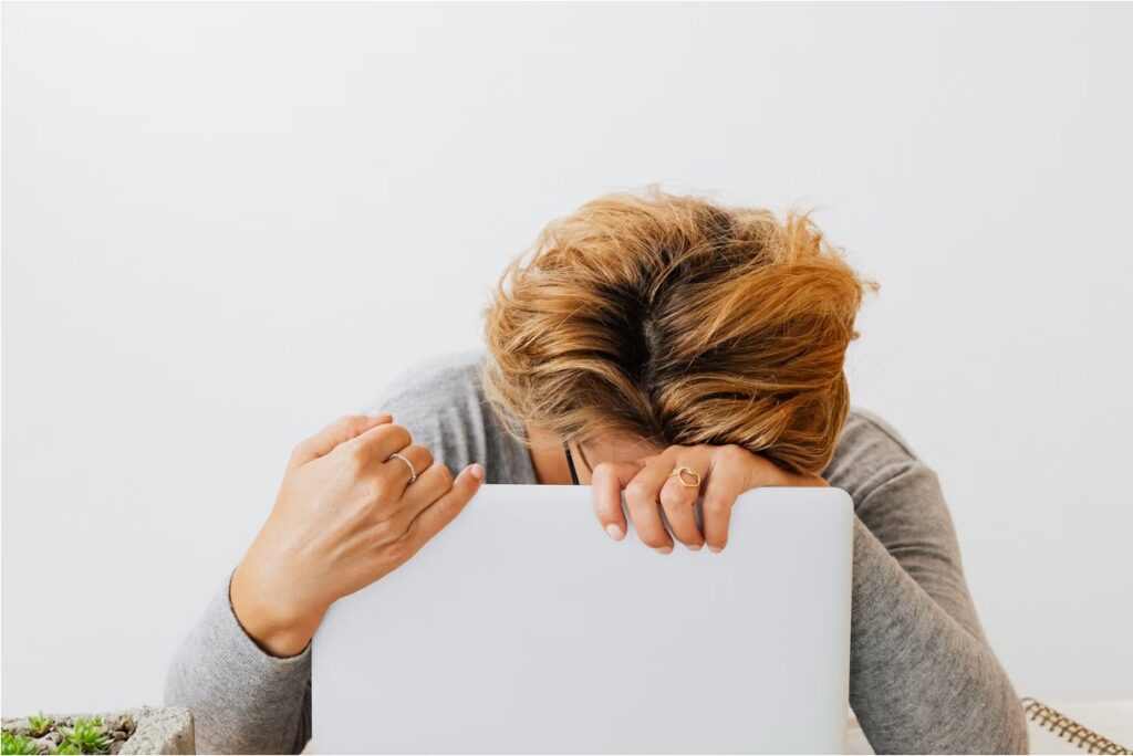 Teen resting their head face down on a laptop, appearing exhausted and overwhelmed
