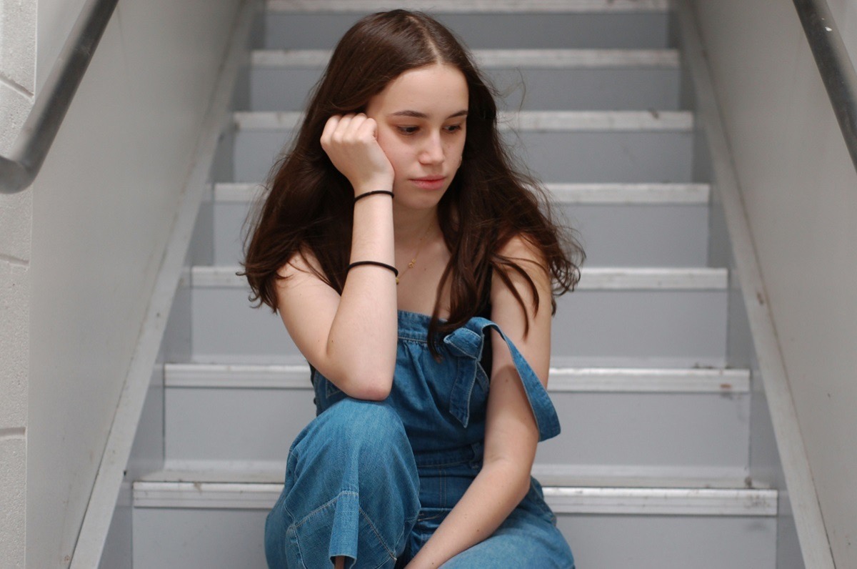 Teen sitting alone on stairs with a withdrawn expression