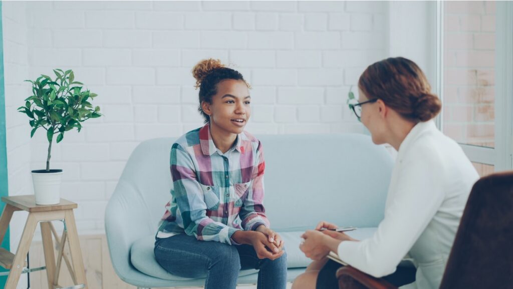 Teen sitting on a couch talking with a therapist taking notes during a counseling session