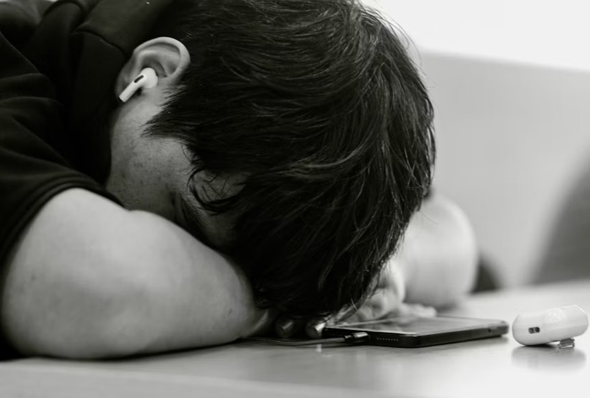Teen with head resting on table looking sad.