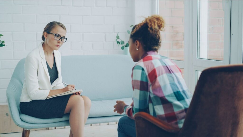 Therapy session between a teen girl and a therapist in a calm, white room