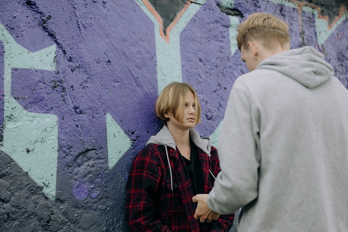 Two teenage boys in a tense standoff against a graffiti wall, one with a cold, unflinching expression