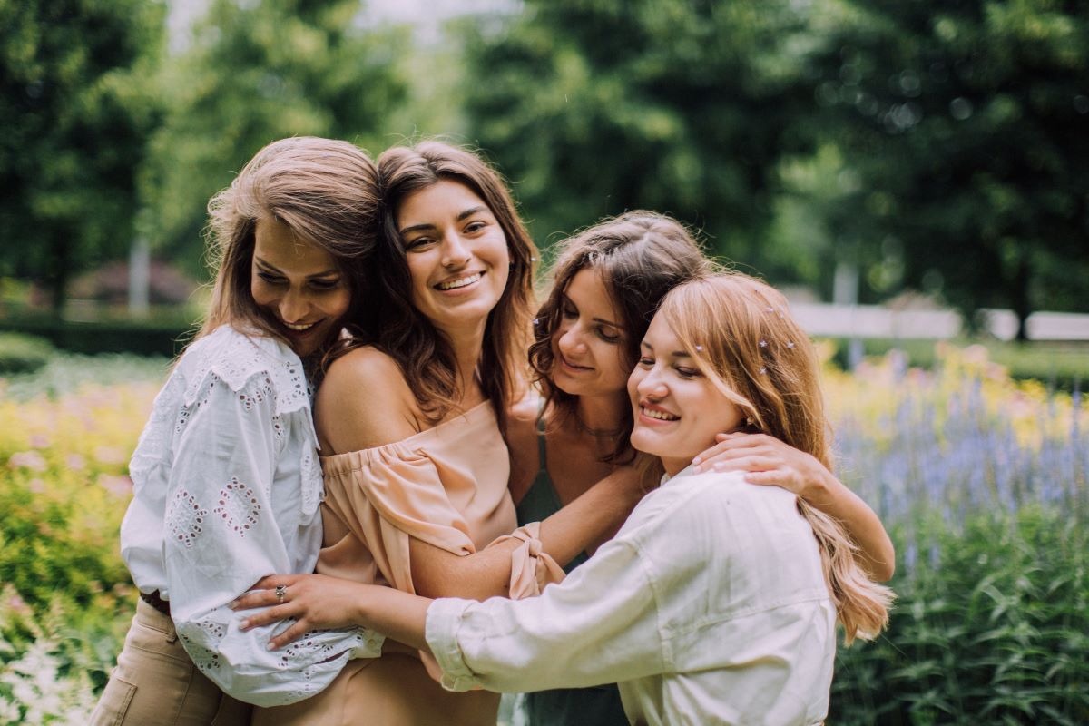 Four teen girls smiling and embracing outdoors, representing peer connection and recovery support in teen girls rehab