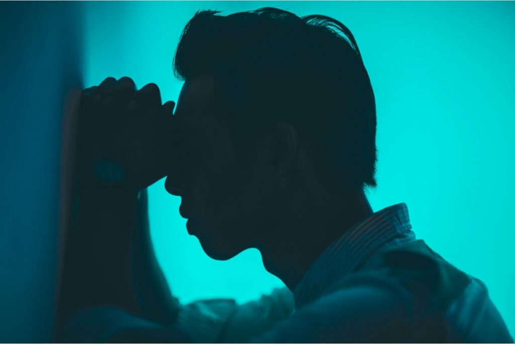 Man feeling depressed, with his arms on the wall and his head leaning on his hands