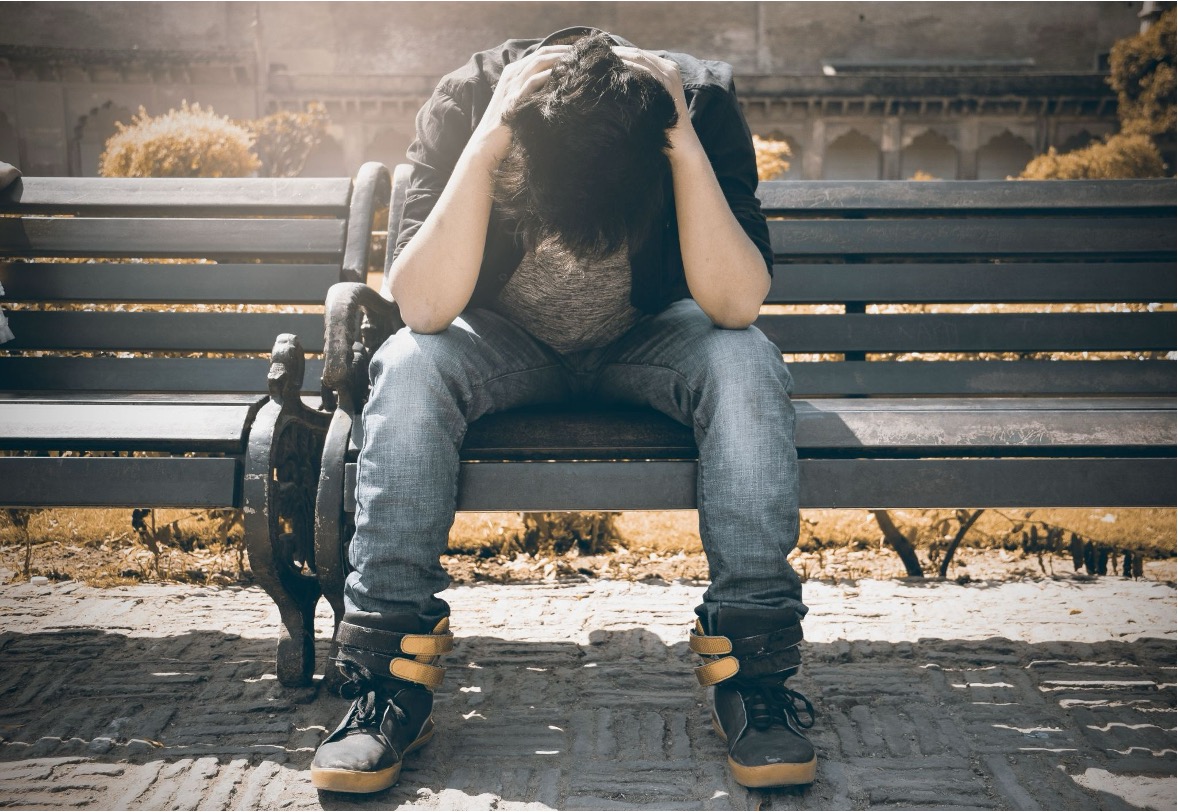 Stressed teenager sitting on a park bench with his hands on his head