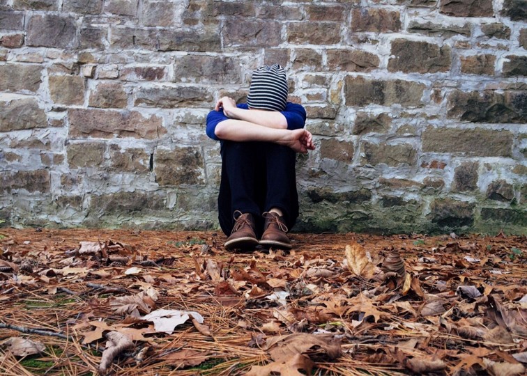 Teen curling up with his head on his arms and leaning against a brick wall