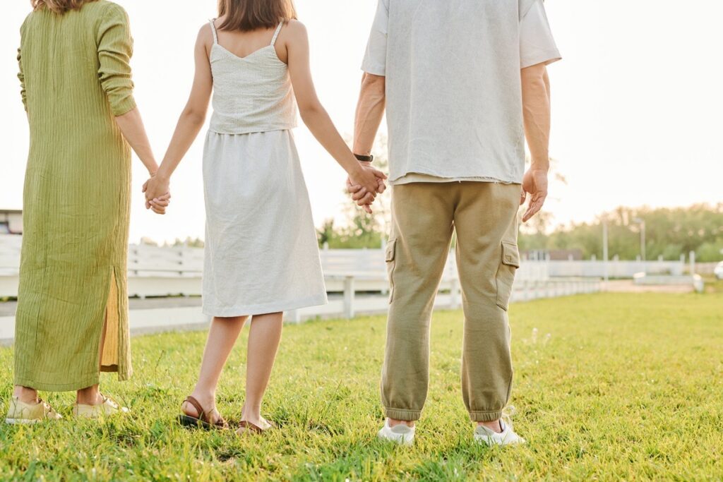 Teen holding hands with both parents outdoors, illustrating family involvement in teen rehab recovery near Irving, TX