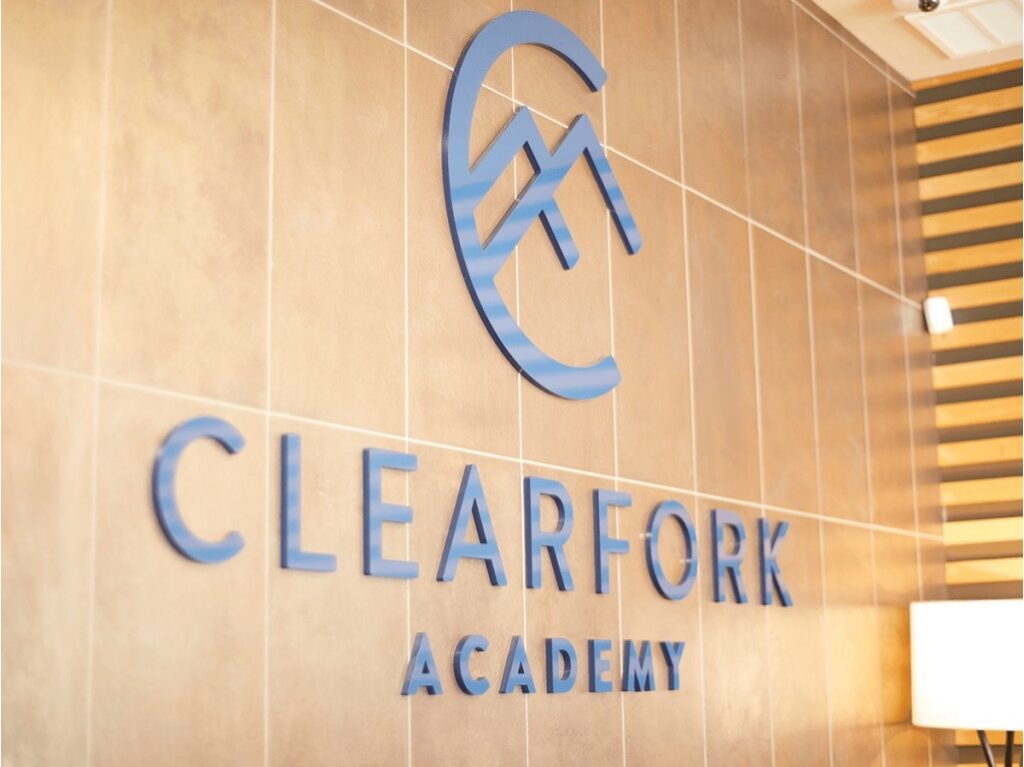 Blue “CLEARFORK ACADEMY” logo with a mountain emblem mounted on a tiled wall at the treatment center