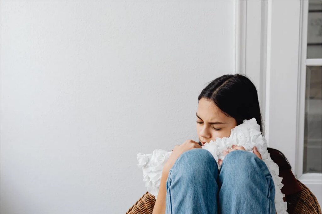 Distressed teen girl hugging a white ruffled pillow to her knees, reflecting depression linked to vaping