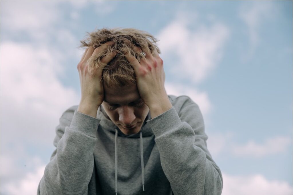 Distressed teen in a gray hoodie clutching his head, reflecting the anxiety of nicotine withdrawal.