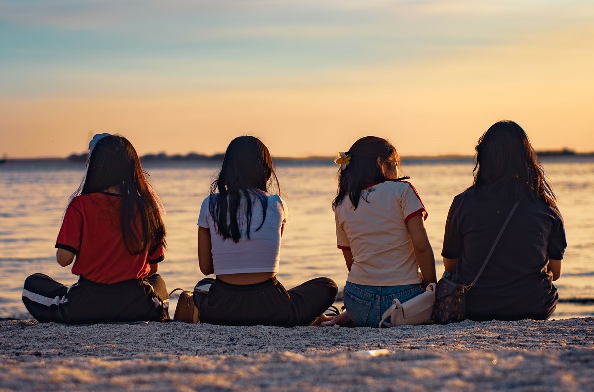 Four teen girls sitting together on a beach at sunset, reflecting the peer support that teen drug rehab in Garland can offer